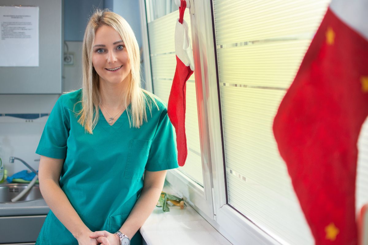 Stocking Stuffers to Brighten Your Smile Blonde woman in teal scrubs smiling in dental office with Canadian flag visible.